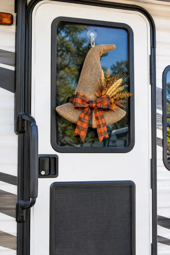 Burlap witch hat wreath hanging from a suction cup hook on an RV exterior entry door window.